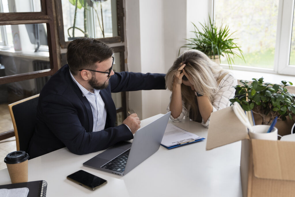 Man consoling stressed woman in office with documents and laptop