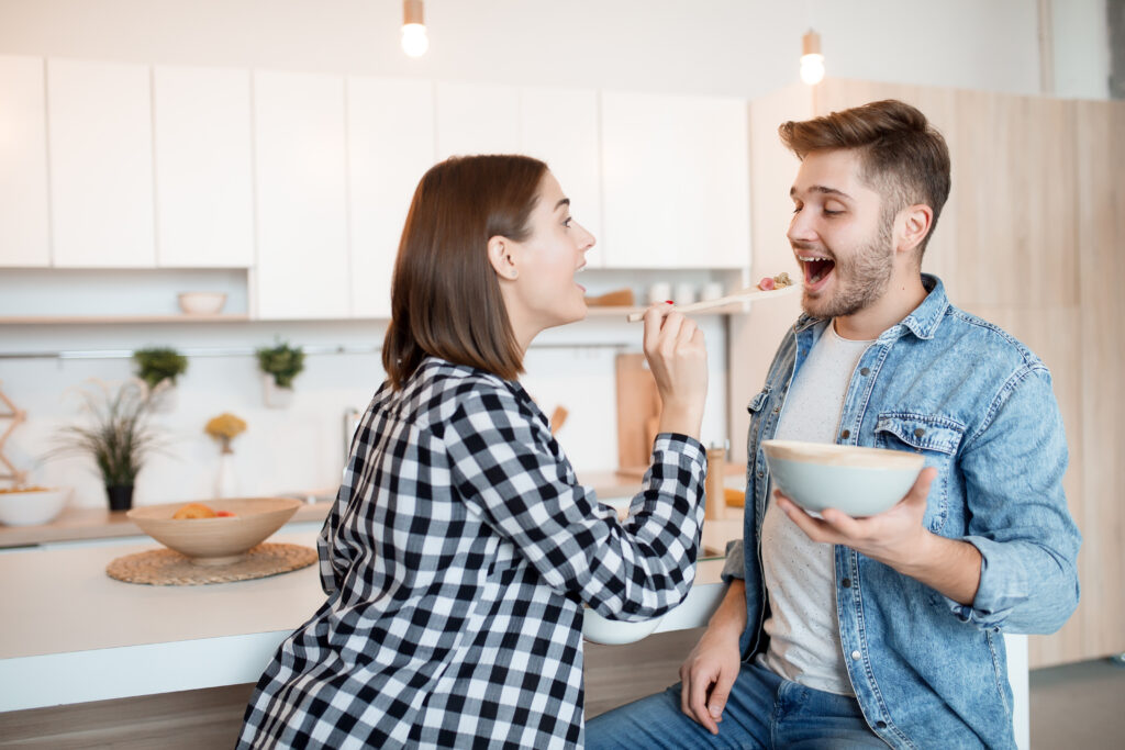 young happy man and woman in kitchen, eating breakfast, couple together in morning, smiling